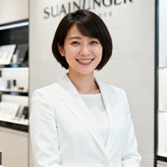 一位留着短发的品牌赞助商女性代表的正面半身照，她穿着干练的白色职业装，面带微笑，背景为品牌展示区的整洁墙面。